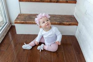 Little crawling baby girl one year old siting on floor in bright light living room near window smiling and laughing photo