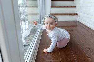 pequeña niña gateando de un año sentada en el suelo con luz brillante en la sala de estar cerca de la ventana sonriendo y riendo foto