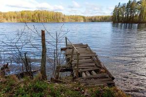 Forest lake or river on summer day and old rustic wooden dock or pier photo