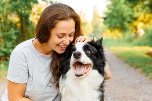 Smiling young attractive woman playing with cute puppy dog border collie on summer outdoor background. Girl holding embracing hugging dog friend. Pet care and animals concept. photo