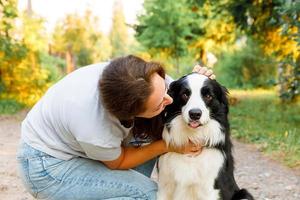 Young attractive woman playing with cute puppy dog border collie on summer outdoor background. Girl kissing holding embracing hugging dog friend. Pet care and animals concept. photo