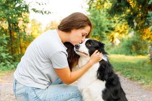 Young attractive woman playing with cute puppy dog border collie on summer outdoor background. Girl kissing holding embracing hugging dog friend. Pet care and animals concept. photo