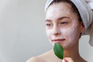 Woman face with green leaf and cream or nourishing mask photo