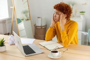 African woman touching temples experiencing stress. Girl at home office tired of working feeling headache sick rubbing temples forehead. Long laptop usage computer vision syndrome. Office syndrome. photo