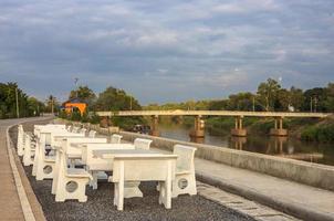 Views of rows of white marble tables and chairs are laid out on a paved stone floor, paving a way. photo