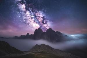 Milky Way over mountains in fog at night in summer. Landscape with foggy alpine mountain valley photo