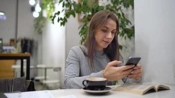 hermosa mujer gasta su hora en un café utilizando teléfono inteligente y Bebiendo café video