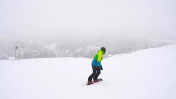 View from height to man is riding a snowboard on a snow-covered field on a cable behind a car video