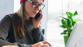 hermosa joven mujer trabajando y Hablando en un teléfono inteligente en un café video