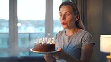 Happy excited woman making cherished wish and blowing candles on holiday cake, celebrating birthday at home, slow motion video
