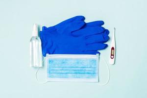 Top view of alcohol hand sanitizer, latex gloves, digital thermometer and medical mask on blue background. Virus protection equipment concept with copy space photo