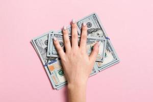 Female hand lying on stack of one hundred dollar bills on colorful background. Saving money and wellbeing concept photo