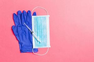 Top view of disposable surgical mask, pair of latex medical gloves and syringe on pink background. Virus protection concept with copy space photo