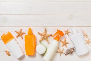 botellas de protección solar con conchas marinas sobre una mesa de madera blanca. vista superior de accesorios de salud de viaje foto