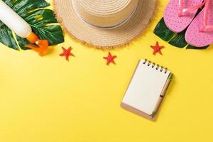 Beach accessories with straw hat, sunscreen bottle and seastar on yellow background top view with copy space photo