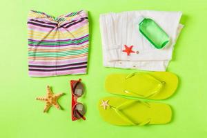 Flat lay composition with green Beach accessories on green color background. Summer holiday background. Vacation and travel items top view photo