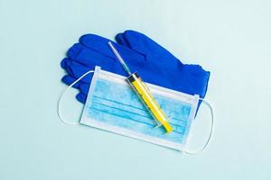 Top view of disposable surgical mask, pair of latex medical gloves and syringe on blue background. Virus protection concept with copy space photo
