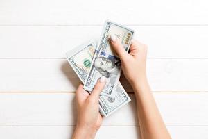 Female hand giving one hundred dollar banknotes on wooden background. Top view of wealth concept photo