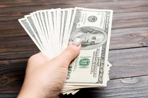 Perspective view of female hand holding a fan of money on wooden background. One hundred dollar bills. Credit and debt concept photo