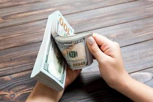 Perspective view of a businesswoman's hands counting one hundred dollar banknotes on wooden background. Success and wealth concept photo