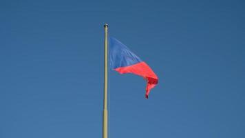 National flag of the Czech Republic, tricolor of red, white and blue. The Czech flag on a flagpole flutters in the wind against a blue sky. video