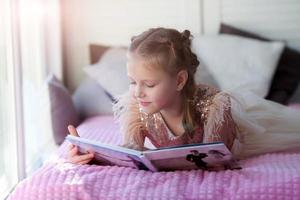 A little beautiful girl lies on the bed and looks at her parent is wedding photo album.