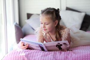 A little beautiful girl lies on the bed and looks at her parent is wedding photo album.