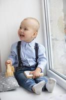 pequeño bebé cerca el ventana. el alegre niño con un juguete se sienta en un ventana umbral. foto