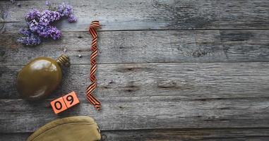 Flask, george ribbon, garrison cap and lilacs on a wooden background. Wooden calendar with date 9 May. Victory Day. Copy space. photo