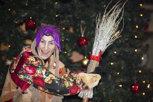 baba yaga con un Escoba en el antecedentes de el Navidad árbol. foto