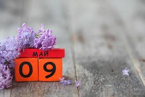 Wooden calendar with Russian text May 9 and a bouquet of lilacs on a wooden background. Victory Day. Copy space. photo