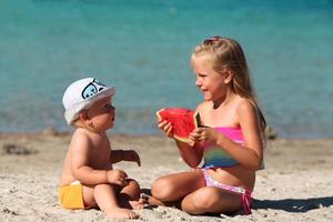 Sister and brother on the beach with watermelon. Girl and little boy are eating on the beach. The children had a picnic by the sea. photo