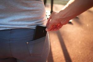 de cerca de un hombre es mano roba un móvil teléfono con un pantalones bolsillo. delito, carterista en el calle foto