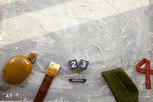 Flask, cap , george ribbon, soldier belt with a five-pointed star with a hammer and sickle and a wooden calendar with the date February 23. Fatherland defender day. Text in Russian photo