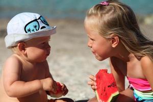 Portrait of children of sister and brother on the beach with watermelon. Girl and little boy are eating on the beach. The children had a picnic by the sea. photo