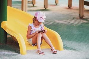 The girl sits on the playground and plays games on the phone. Internet addiction, loneliness. photo