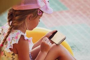 The girl sits on the playground and plays games on the phone. Internet addiction, loneliness. photo