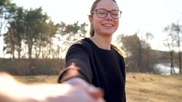 Follow me - happy young woman pulling guy's hand. Hand in hand walking to the bank of the river, slow motion video