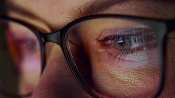 Woman in glasses looking on the monitor and surfing Internet. The monitor screen is reflected in the glasses video