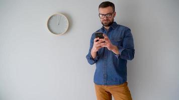 barbudo homem usando Smartphone contra uma cinzento parede com uma relógio video