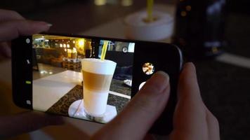 Girl makes a photo of coffee on a smartphone in a cafe close up video
