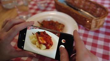 Girl makes a photo of meal on a smartphone in a cafe close up video