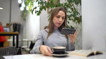 Beautiful woman spends her time in a cafe reading a book, talking on the phone and drinking coffee video