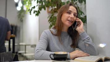 mooi vrouw besteedt haar tijd in een cafe lezing een boek, pratend Aan de telefoon en drinken koffie video