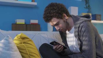 Jeune homme mensonge sur le canapé dépense une lot de temps avec le sien téléphone intelligent, obtient intoxiqué à il. téléphone intoxiqué Jeune homme mensonge sur canapé à maison, à la recherche à cellule téléphone, surfant social médias, SMS. video