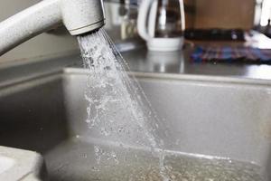 Water is pouring from a faucet. Water tap on the background of the kitchen. Water saving. photo