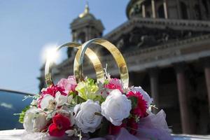 Wedding day. Wedding rings on a car with a bouquet on the background of a beautiful building. Betrothal. photo