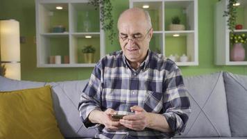 vecchio uomo con bicchieri avendo difficoltà utilizzando un' smartphone. vecchio uomo guardare a il suo smartphone nel il suo naturale stato a casa. video