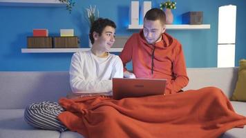 Two brothers browsing social media and dating sites on a laptop. Two brothers who can get along and get along are at home together using a laptop to browse online applications. video