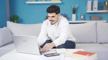 Home office worker receiving a phone message, stopping his work. The young man, who does not want to work, takes a break from his work and has fun when he receives a message on his phone. video